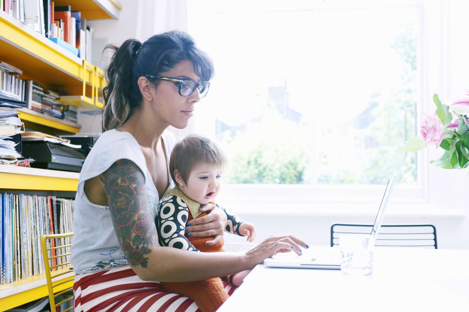 有袖子纹身的女人抱着孩子使用笔记本电脑