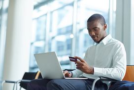 Young man in white shirt sitting at airport making an online purchase with credit card