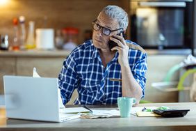 person in blue checkered shirt on the phone with a stressed look on their face