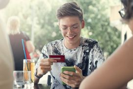 十几岁的男孩微笑着用他的第一张信用卡支付家庭午餐＂width=