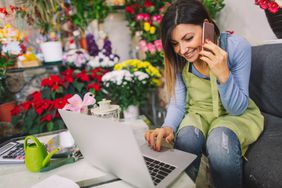 女花店老板坐在花旁，用手机看电脑
