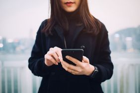 年轻女子用模糊的脸拿着手机并在外面使用。