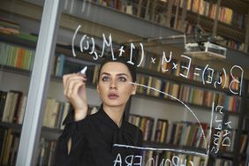 女人一个清晰的玻璃黑板上写数学计算在一个办公室