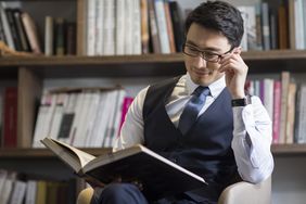 戴眼镜的男人穿着正装衬衫、领带和背心在读一本书