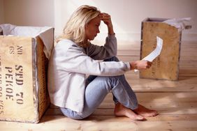 一个女人在空荡荡的公寓里看着一份租赁协议，旁边放着箱子