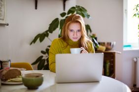 年轻女子坐在桌旁，看着她的笔记本电脑和喝咖啡。女性在家里使用笔记本电脑。＂>
          </noscript>
         </div>
        </div>
       </div>
       <div class=
