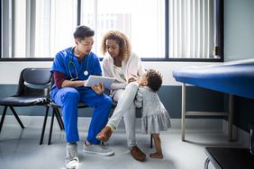 A nurse shows a digital tablet to a mother and toddler in a hospital