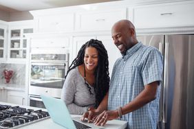 一对微笑的夫妇在厨房柜台上用笔记本电脑工作