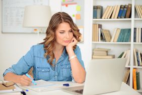 一个女人坐在家里办公室的电脑前写笔记