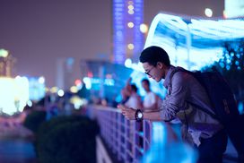 一个年轻的商人在一座有灯的桥上看手机