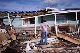 一名男子站在一座被毁的房子前，双手叉腰。