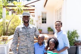 一个士兵和他的家人站在一所房子前＂width=