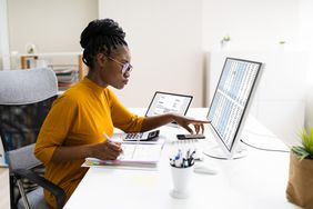 一名妇女在台式电脑前用打开的活页夹处理税务问题