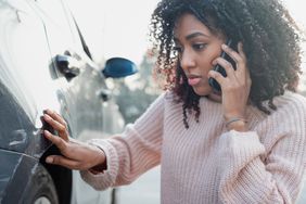 一名女子检查她汽车后挡泥板的损坏情况，并打电话给她的保险公司