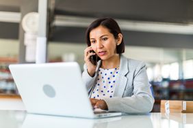 person with short hair in star-designed shirt talking on phone in front of laptop