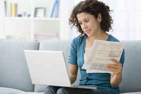 一位女士一边拿着一些财务报表，一边在笔记本电脑上工作