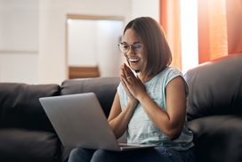 一位女士坐在豪华的皮沙发上，膝上放着一台笔记本电脑，微笑着鼓掌，看着屏幕上的东西。＂width=