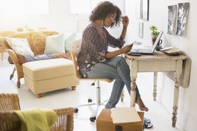 女人坐在家里的办公桌前，看着笔记本电脑前的应用程序