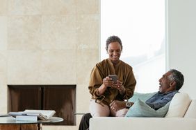 微笑的男人看着女性伴侣的智能手机坐在家里的大腿上
