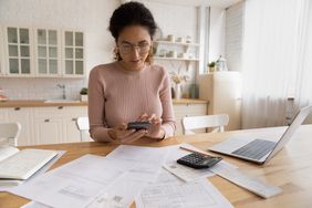 一个女人用她的计算器和电话在餐桌上做税。