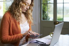 一个女人用计算器和电脑为不定期的开支制定预算