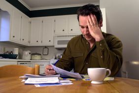一个紧张的男人坐在厨房桌子前看着一堆账单。