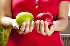 一个女人一手拿红苹果，另一只手拿绿苹果，代表养老金和年金利率的比较。