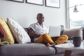 一位房主舒适地坐在沙发上，用笔记本电脑查看反向抵押贷款要求。