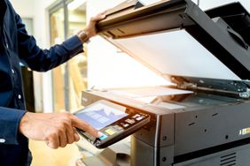 Businessman using an office copier to make duplicates of an advertisement for mailing to clients.