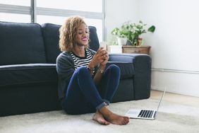 微笑的女人坐在客厅地毯上看着智能手机