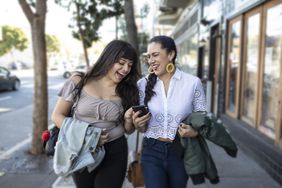 两个女人走在街上一边笑一边看手机
