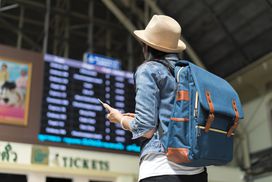 徒步旅行的年轻女子旅游看了看头顶的董事会在机场航班信息终端。”width=