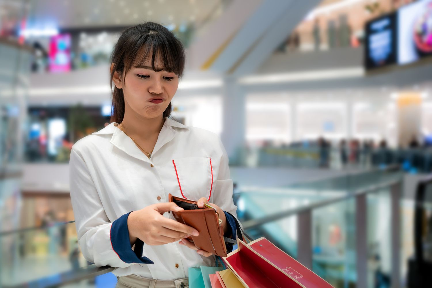 一名年轻女子在商场购物时皱着眉头看钱包