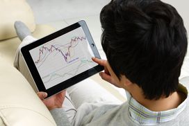 男子在电子平板电脑上看股票市场图表＂width=