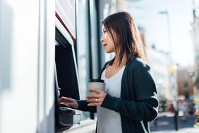 自动取款机前的女人拿着她的银行卡和咖啡杯