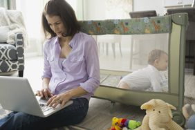 女人在婴儿面前的笔记本电脑坐在地板上游戏围栏