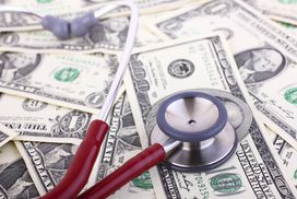 听诊器放在散落的美元钞票上，代表着医疗保健的费用。＂width=