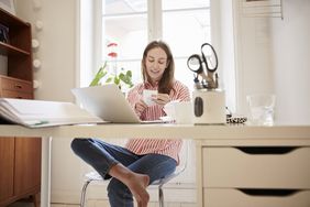 A woman sits at her desk in a bright workroom and prepares her taxes.