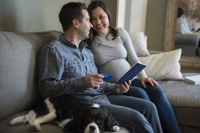一对怀孕的夫妇坐在沙发上，带着狗、平板电脑和信用卡＂>
          </noscript>
         </div>
        </div>
       </div>
       <div class=
