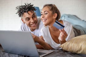 一对夫妻躺在床上用信用卡和笔记本电脑购物，脸上带着微笑