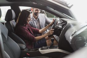 Female customer in driver's seat of new car with a salesperson looking in through the open door