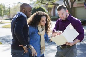 两个房主客户和一个推销员在一个住宅区的街上看一个文件夹。