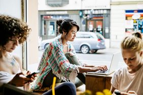 一位时尚的年轻女子正在一家繁忙的咖啡馆里工作，她坐在窗边用笔记本电脑。