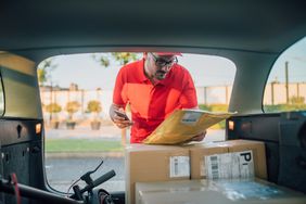一名身穿红色衬衫、头戴红色棒球帽的男子在一辆小型货车或旅行车的后面查看包裹。