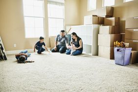一家人坐在新家的地板上，身后是移动的箱子。