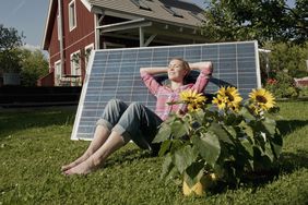 妇女在花园放松与太阳能电池板在生态友好的家