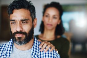 A man looking distressed with a woman comforting him with her hand on her shoulder