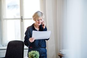女人用智能手机在家庭办公室工作，打电话。