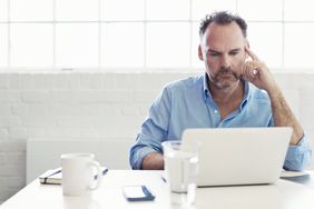 一个穿着有领衬衫的男人坐在白色的房间里，在电脑上工作