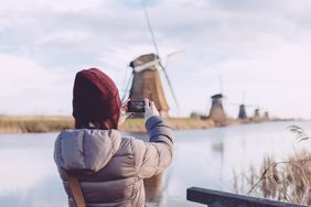 女孩在国外旅行，用智能手机拍下风车的照片